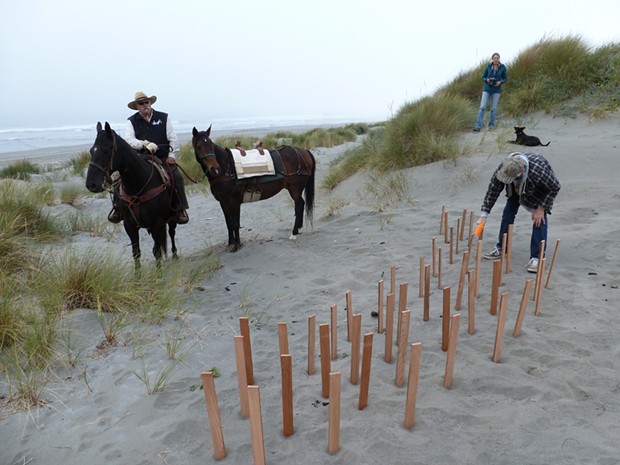 Dennis Mayo of McKinleyville sits horseback while Ray Reel of Manila pounds wooden stakes into the sand.