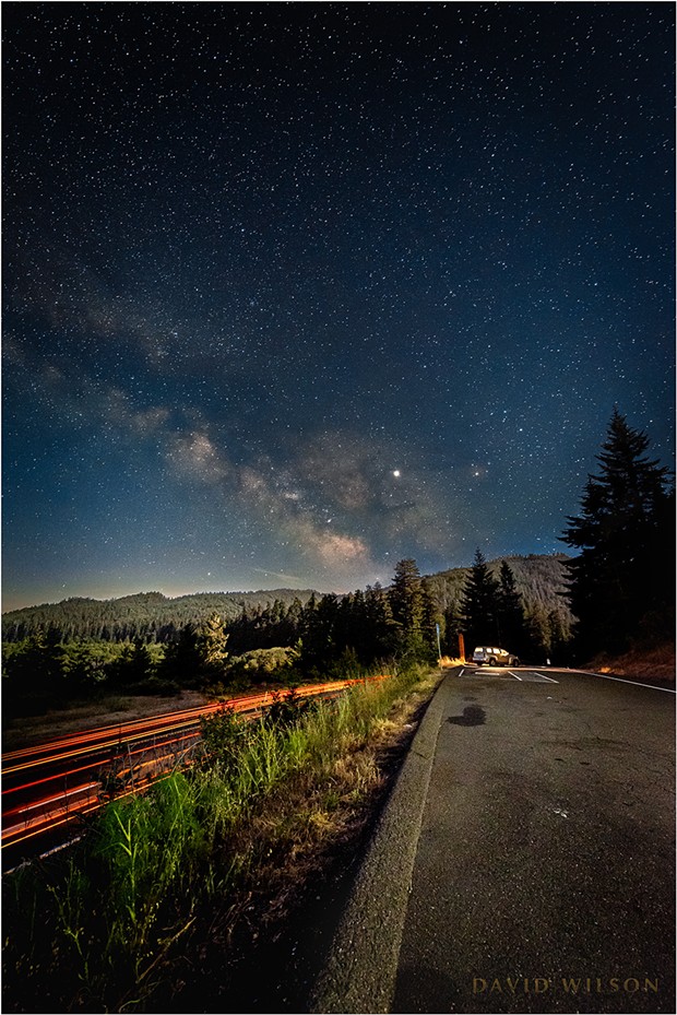 Streaks of humanity pierce the night even as the half moon bathes the forested landscape in its soothing luminance. At the far end a fellow traveler of the night sheltered in their car’s bubble of light. Vista Point, Humboldt County, California. - DAVID WILSON