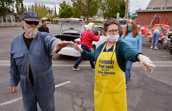 Victoria Salwasser, right, directs Curtis Smith, left, as volunteers distribute food to families in cars at a food bank giveaway held at Easton Presbyterian Church Monday, April 6, 2020 in Easton. - ERIC PAUL ZAMORA, THE FRESNO BEE
