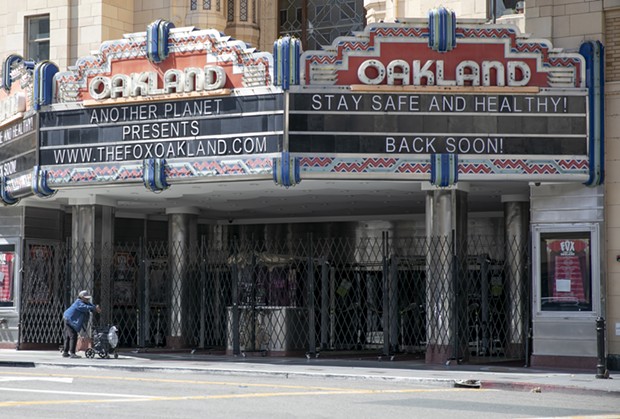 A woman pushes a cart past the shuttered Fox Theater in downtown Oakland on March 25, 2020. - ANNE WERNIKOFF FOR CALMATTERS