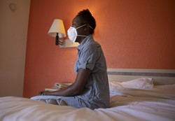 Jamie Burson sits on the bed of her motel room in Farfield on August 4, 2020. Burson, who has been homeless since being evicted in April, says she spends all of her time in her room with the curtains closed. - ANNE WERNIKOFF FOR CALMATTERS