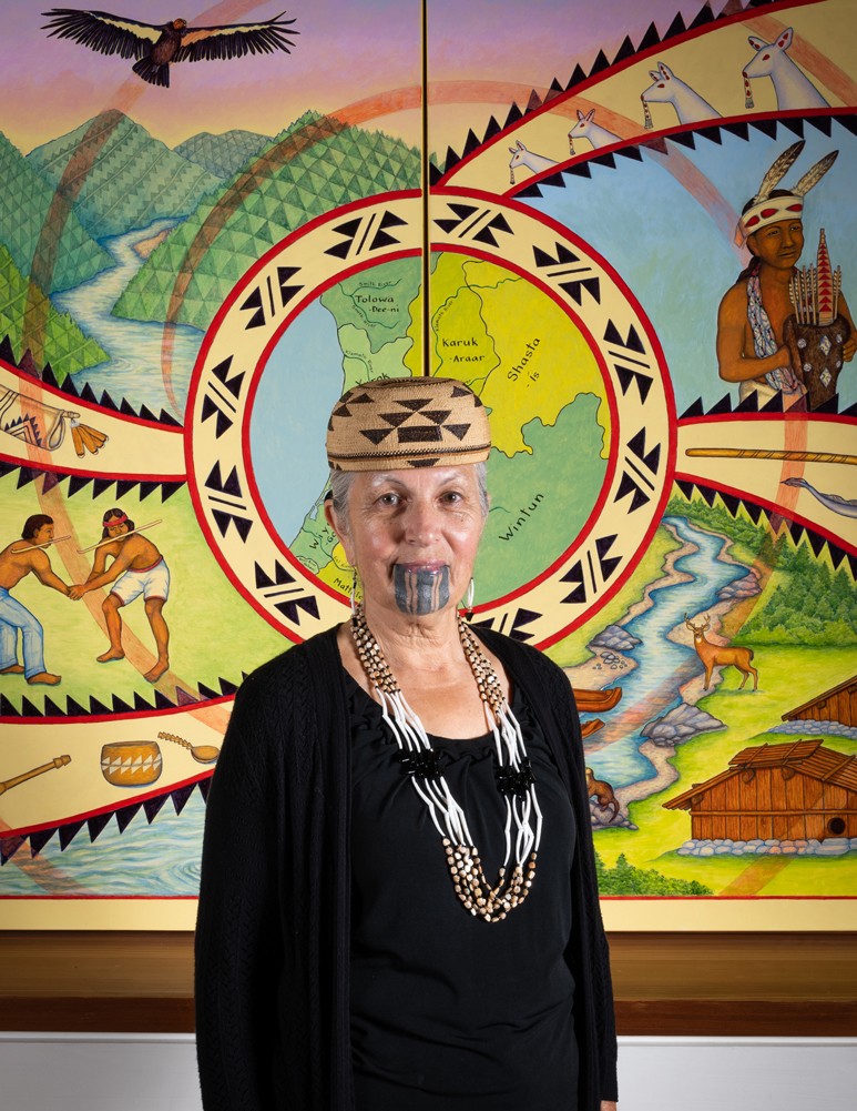 Lyn Risling with her 2019 mural "We Are These People" in the Native American Forum at Cal Poly Humboldt. - PHOTO BY DAVE WOODY