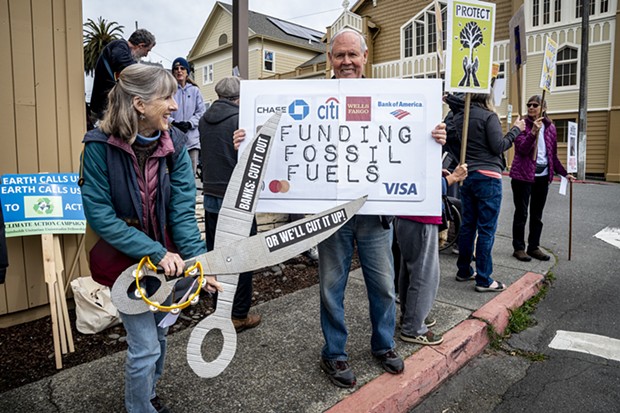 Annette Holland, of Arcata, symbollically cuts up a bank card held by Greg Holland at the Third Act protest in front of Wells Fargo Bank in Arcata. - MARK LARSON