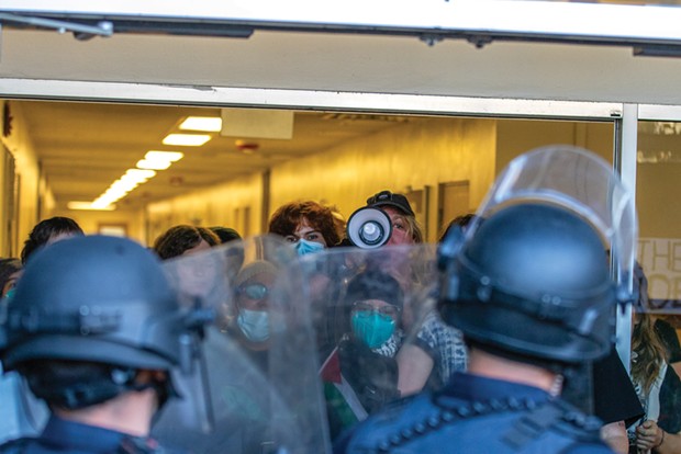A masked protester inside Siemens Hall yells into a megaphone at officers, demanding they leave the scene on April 22. - PHOTO BY ALEXANDER ANDERSON