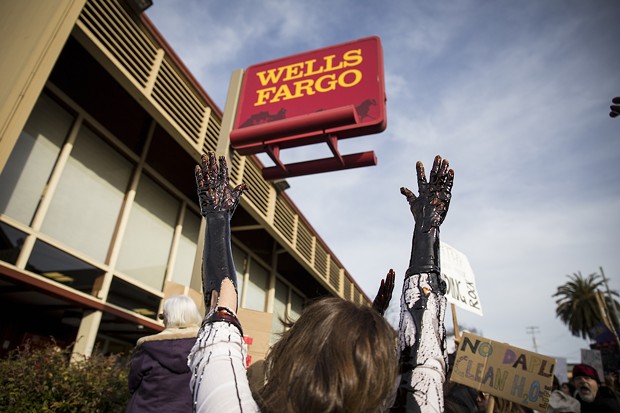 Four protesters brought a large white bucket filled with molasses, which mimicked the look of oil as they let it drip down their arms in protest of Wells Fargo. - SAM ARMANINO