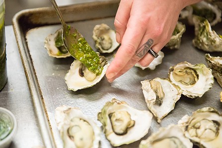Lizette Acuna spoons an Argentinan Chimichurri on a grilled oyster. - MARK MCKENNA