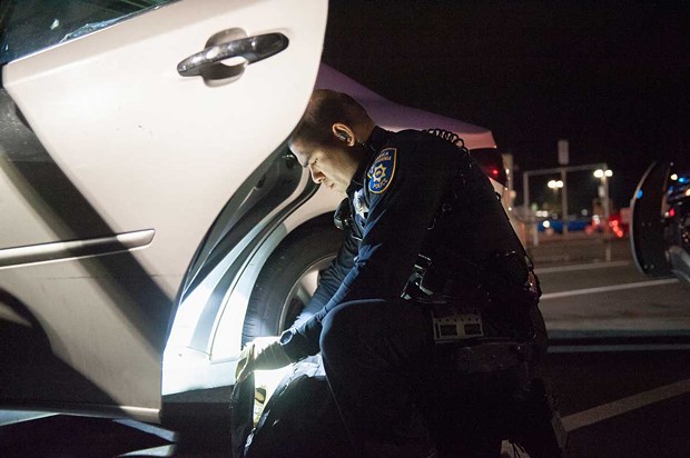 EPD officer Raymond Nunez searches a backpack in the WinCo parking lot. - PHOTO BY MARK MCKENNA