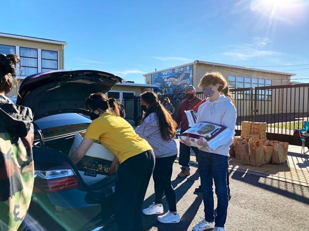 Volunteers, including students from Alice Birney Elementary School, load food into the trunk of a driver delivering to multiple households.