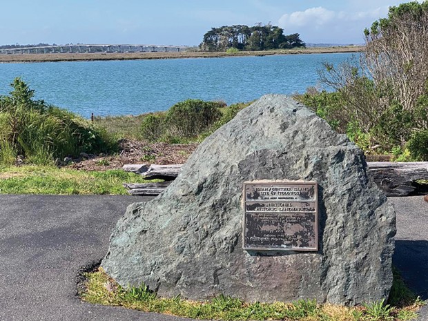 This National Historic Landmark plaque on Woodley Island, with Tuluwat Island (formerly Indian Island) in the background, merely refers to "Indian/Gunther Island, Site 67." No mention is made of the 1860 massacre.
