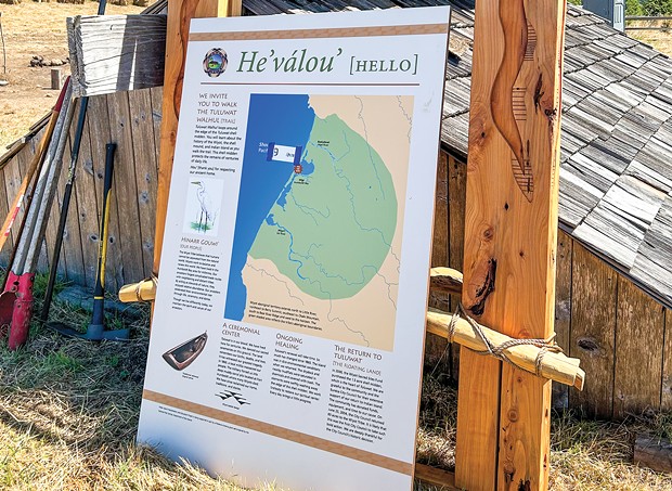 An interpretive sign that will be placed on Tuluwat Island sits next to a redwood plank house at Wiyot Days last month.