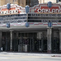 A woman pushes a cart past the shuttered Fox Theater in downtown Oakland on March 25, 2020.