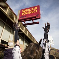 Four protesters brought a large white bucket filled with molasses, which mimicked the look of oil as they let it drip down their arms in protest of Wells Fargo.