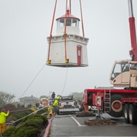 Two workers use ropes to align the lighthouse as it is moved to a trailer.