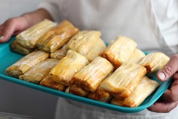 PHOTO BY ANDREA JUAREZ - El Pueblo Market owner Engelberto Tejeda holds a tray of chicken and pork tamales. The two savory options, a vegetarian tamal and sweet corn tamal, are sold at his new Eureka market.