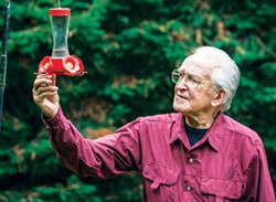 PHOTO BY MARK LARSON - John Hewston inspects a hummingbird feeder in his side yard as the tiny birds were busy feeding on a rainy afternoon.